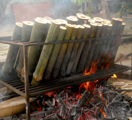 Bamboo tubes filled with sticky rice turning slowly over charcoal