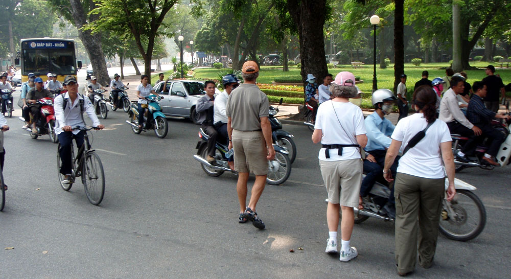 Pedestrians crossing a busy Hanoi street with motorbikes