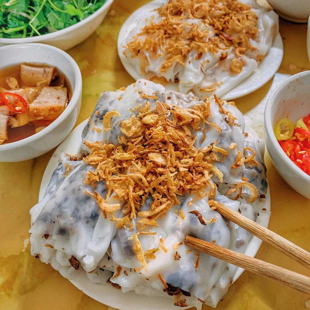 Diner using chopsticks to dip banh cuon into fish sauce in Hanoi