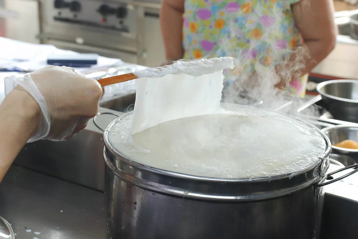 Thin banh cuon rice sheet steaming over stretched cloth