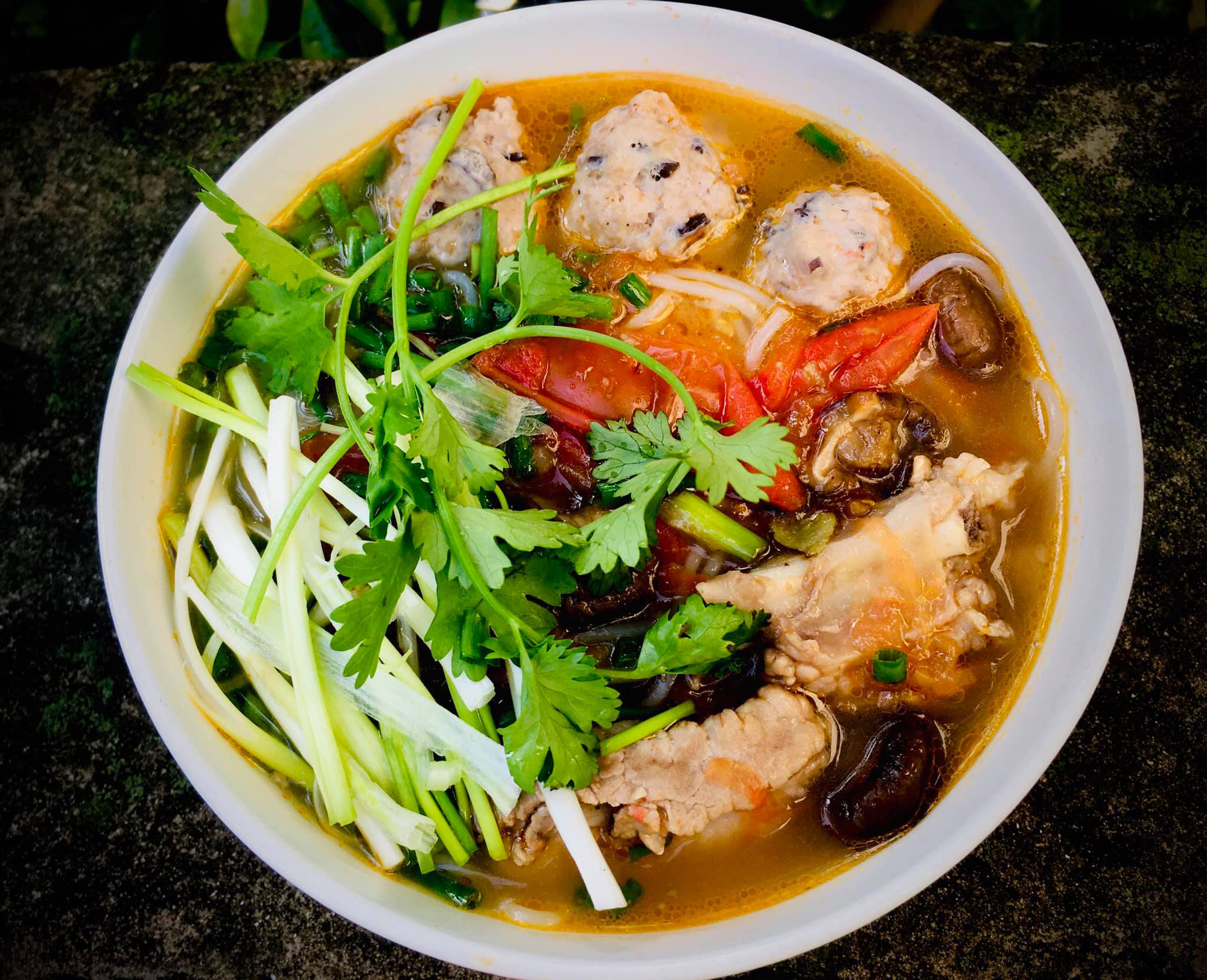 Rice noodles topped with pork ribs, pork meatballs, tomatoes and chopped herbs.
